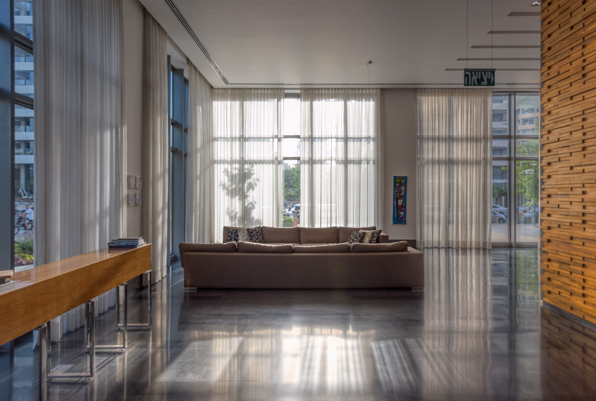 NAM Tower residents’ lounge with communal timber table, sofas and tall windows in Tel Aviv