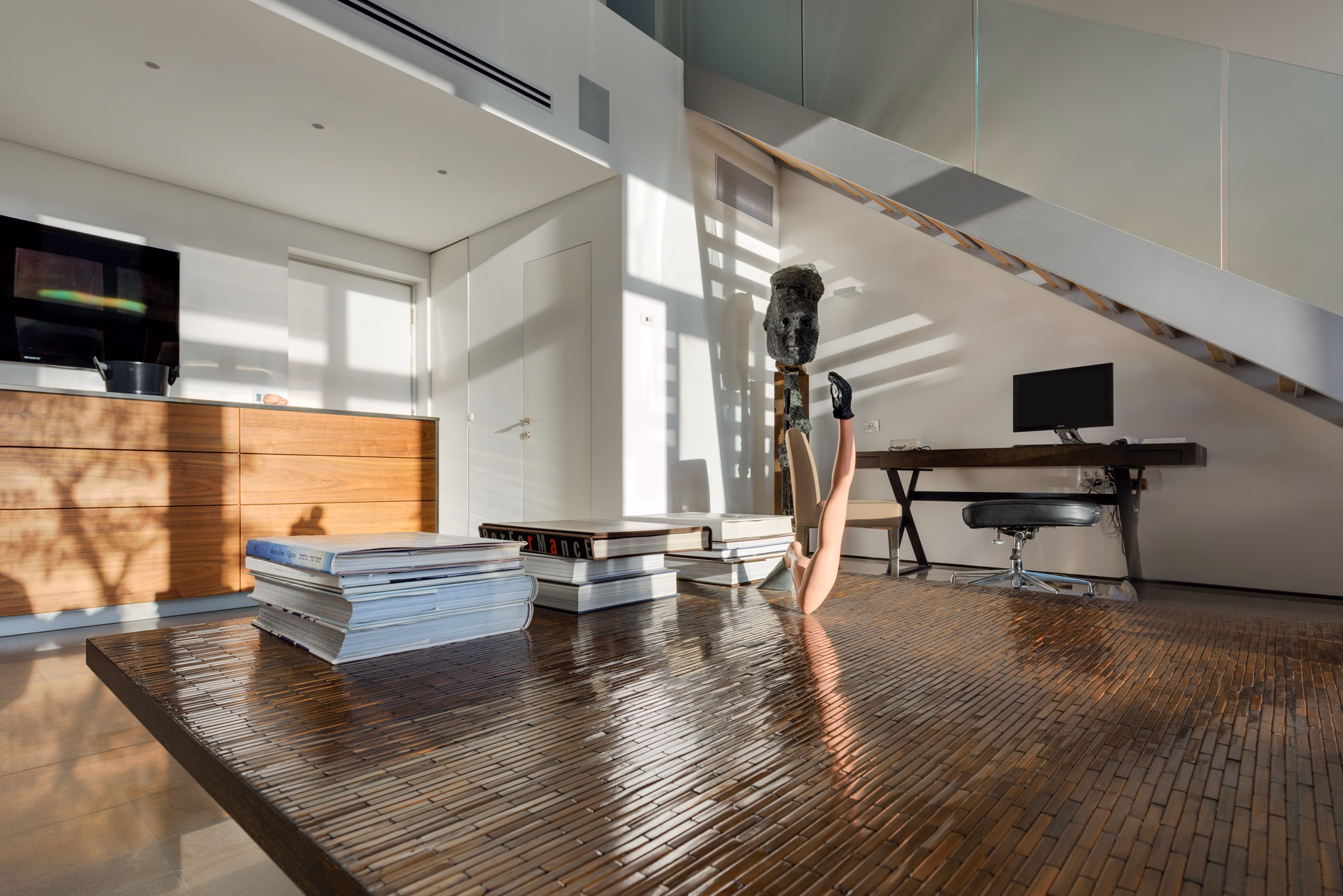 Sunlit loft workspace with sculpture beneath the staircase at NAM Tower in Tel Aviv