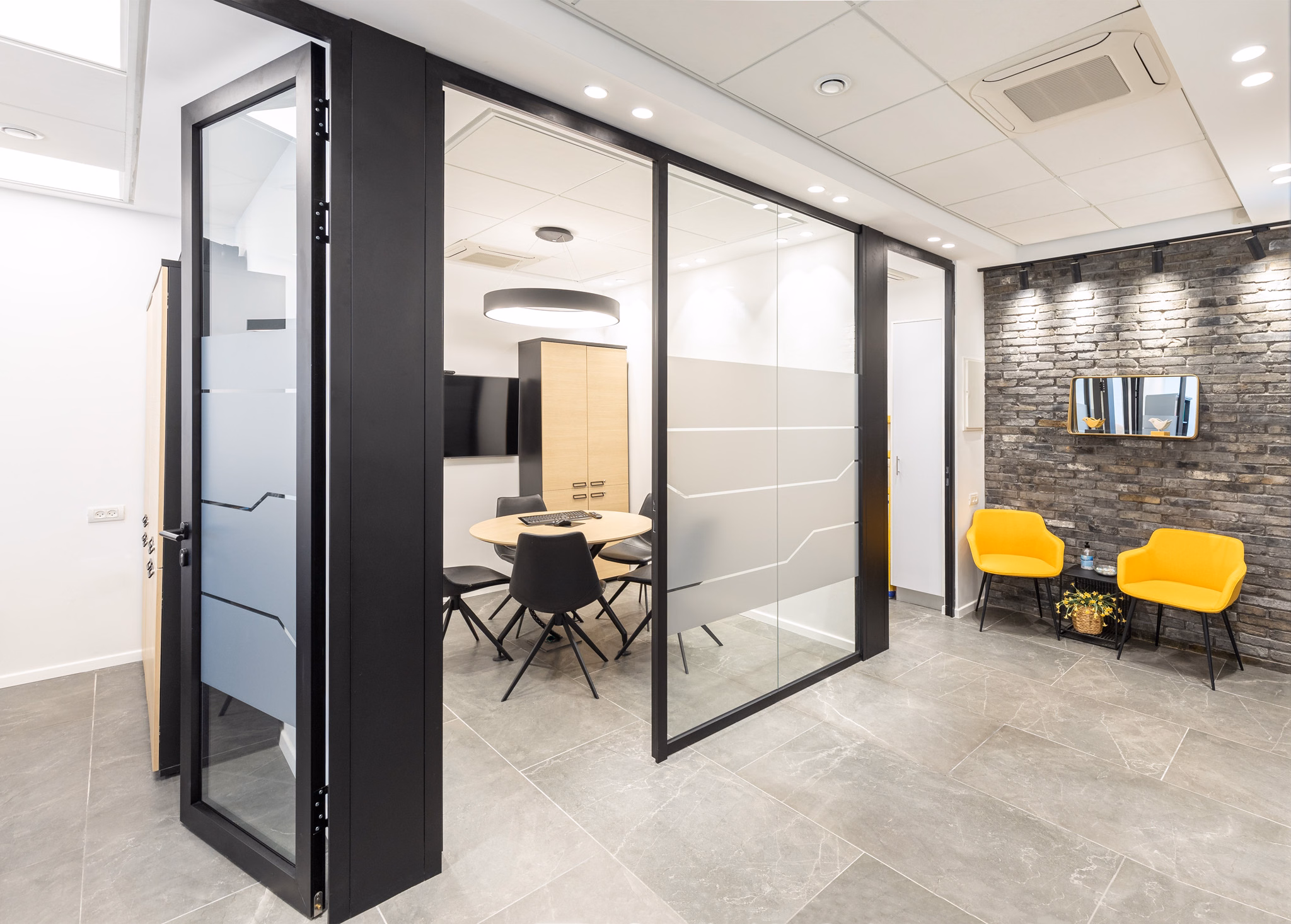 Glass meeting rooms with black frames and yellow lounge chairs at Platinum Four offices in Modiin