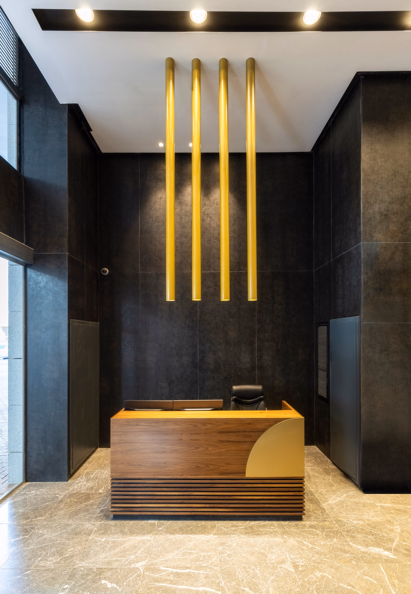 Dark office reception with timber desk and vertical gold light feature at Platinum Four in Modiin